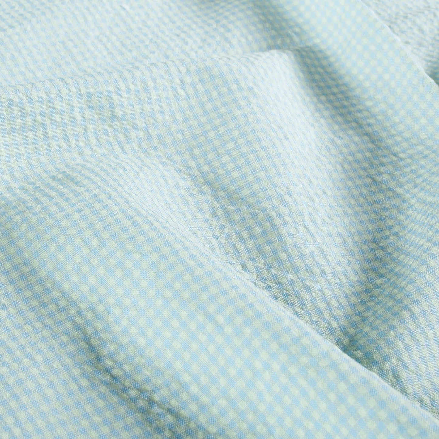A close-up of a light blue and yellow micro-check patterned fabric with soft folds.