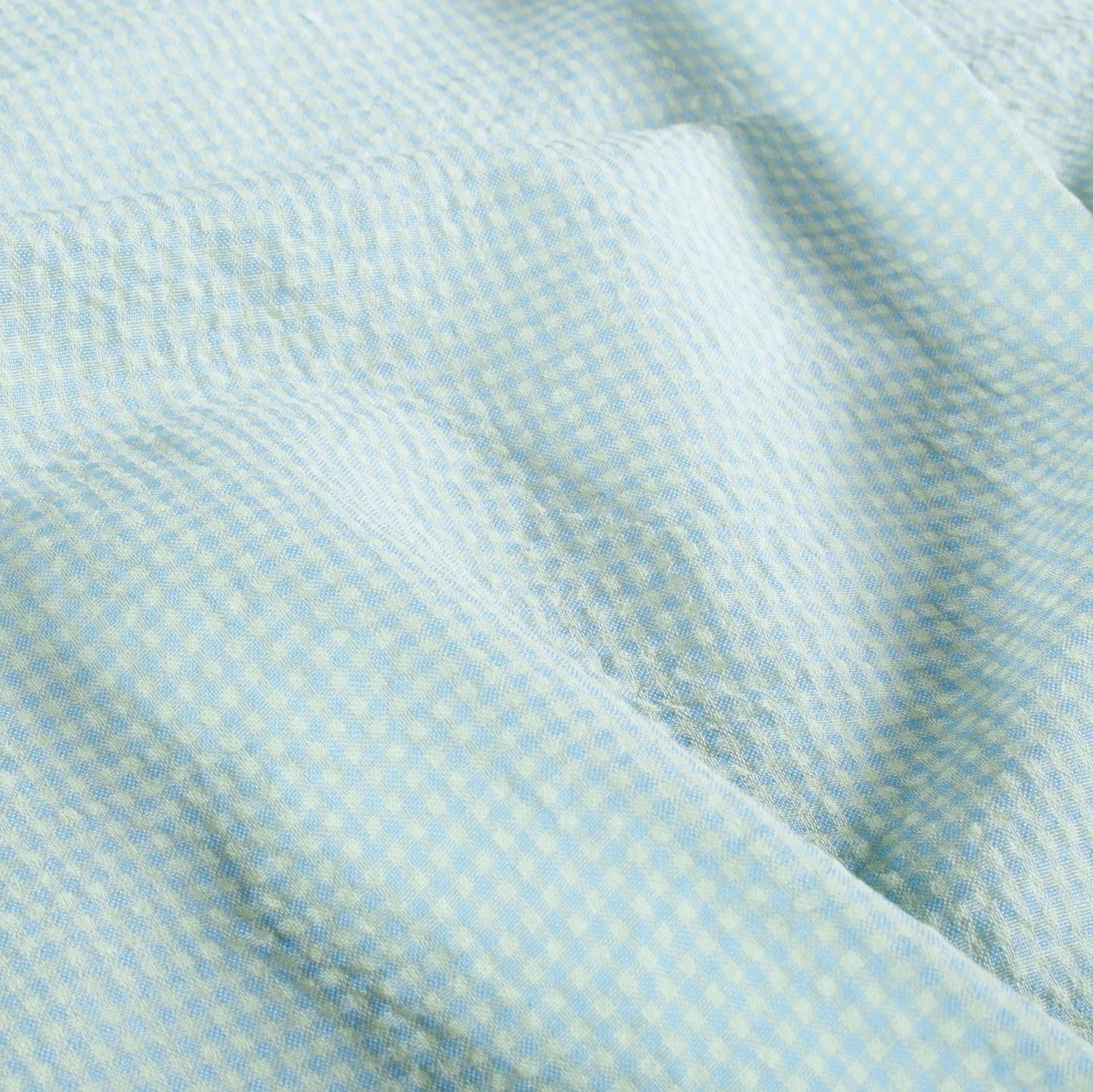 A close-up of a light blue and yellow micro-check patterned fabric with soft folds.
