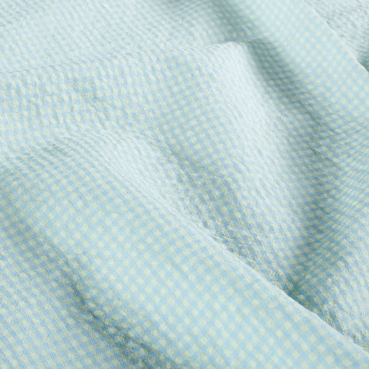 A close-up of a light blue and yellow micro-check patterned fabric with soft folds.
