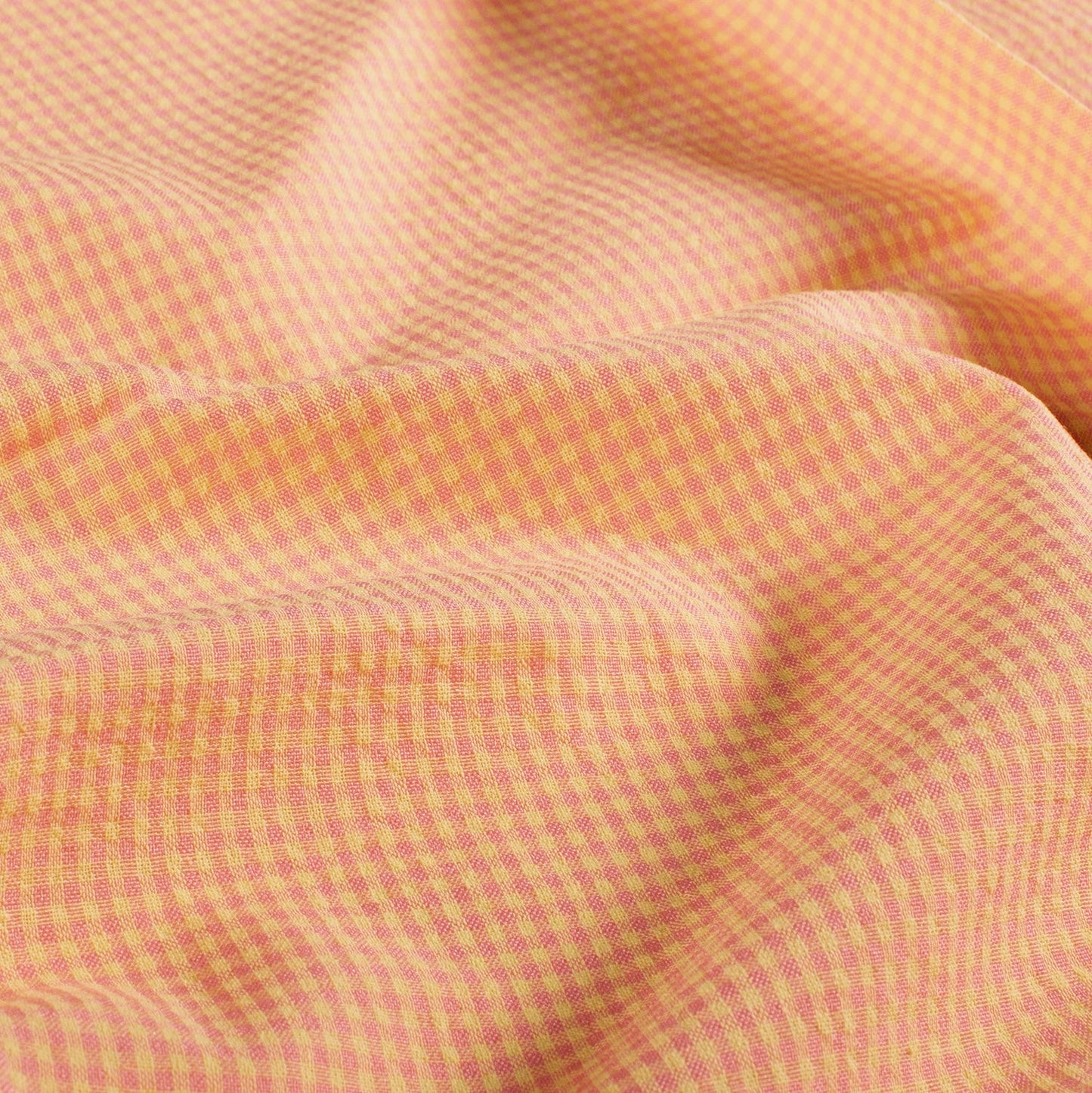 A close-up of draped fabric with a fine gingham check pattern in soft peach and pink.