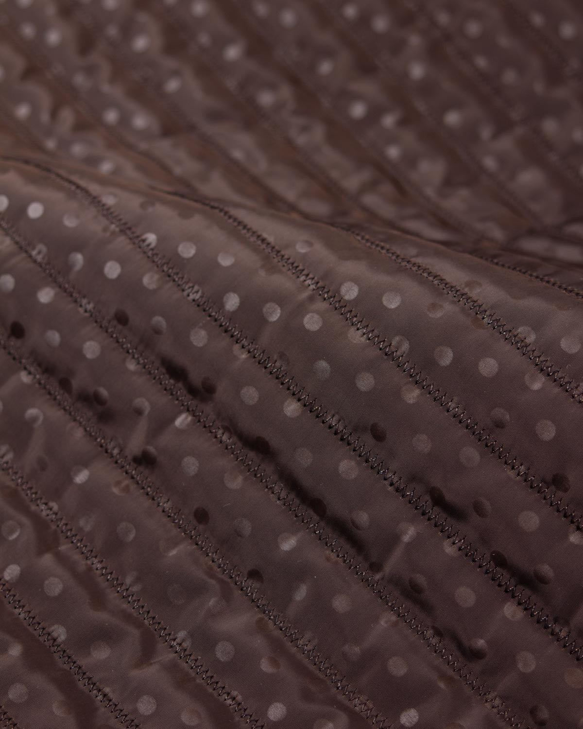 Chocolate brown showerproof quilted fabric with a white polka dot print and zigzag quilting over padded wadding.