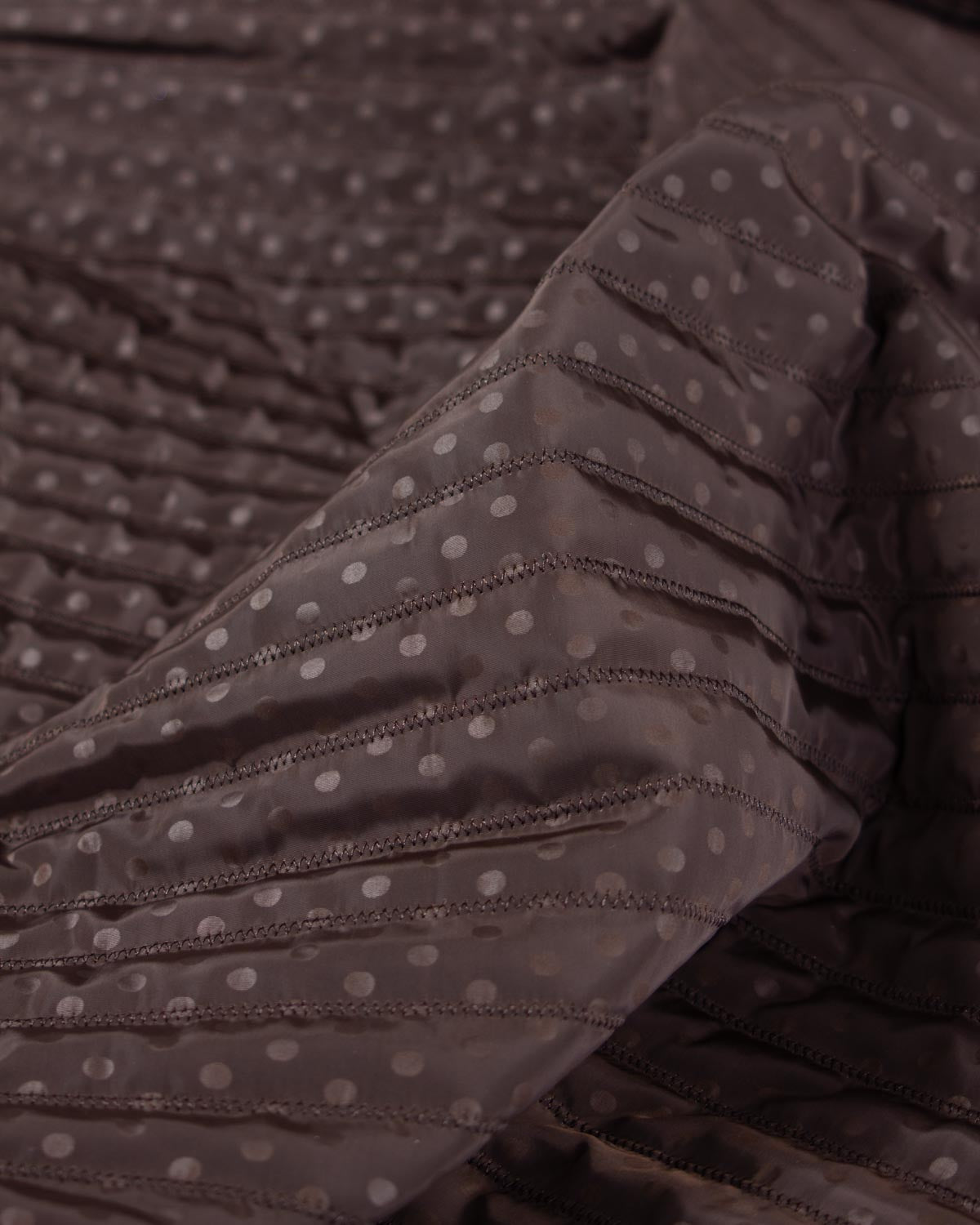 Chocolate brown showerproof quilted fabric with a white polka dot print and zigzag quilting over padded wadding.