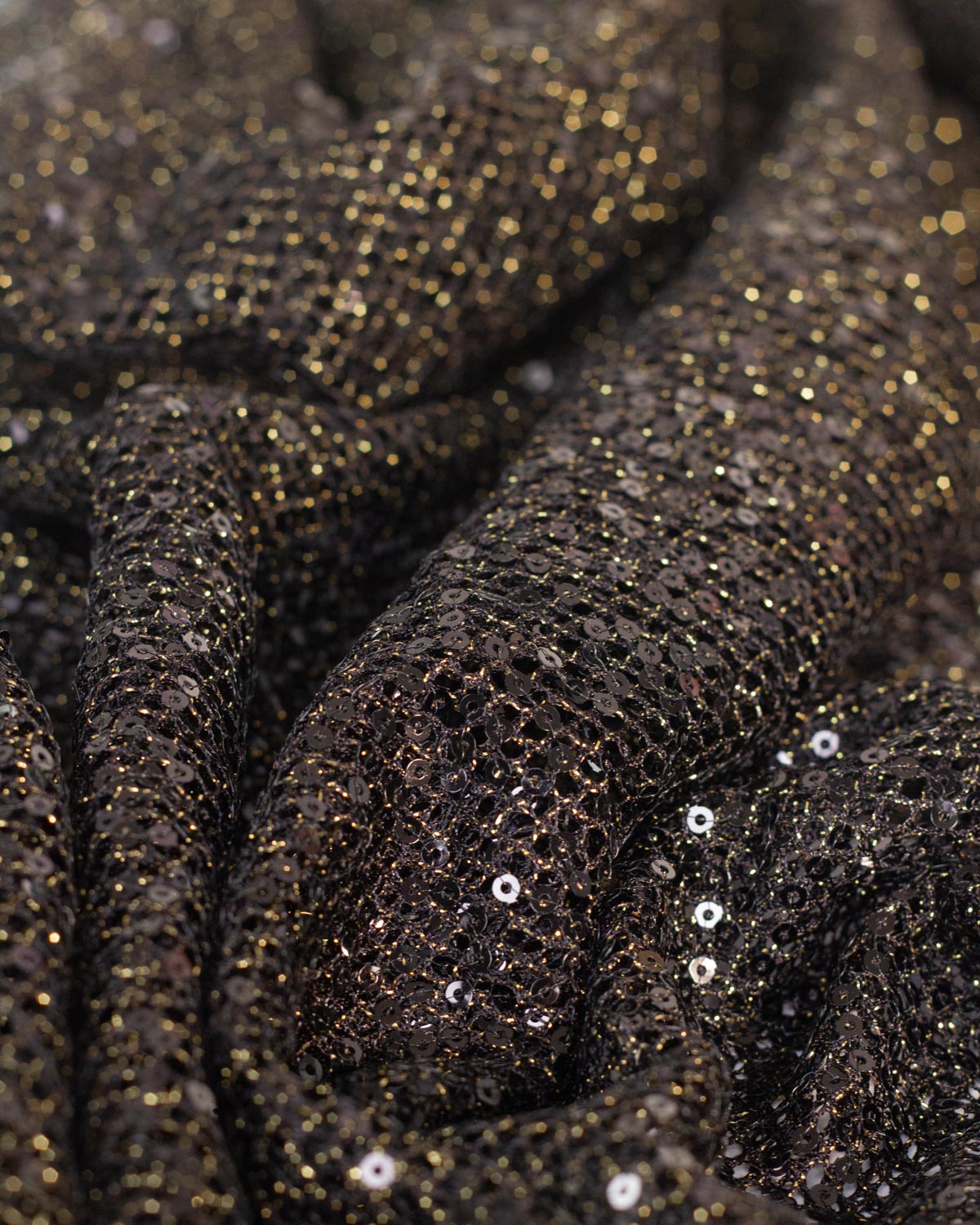 Close-up of a black fishnet tulle sequined fabric with shimmering gold lurex and black sequins draped in soft folds.