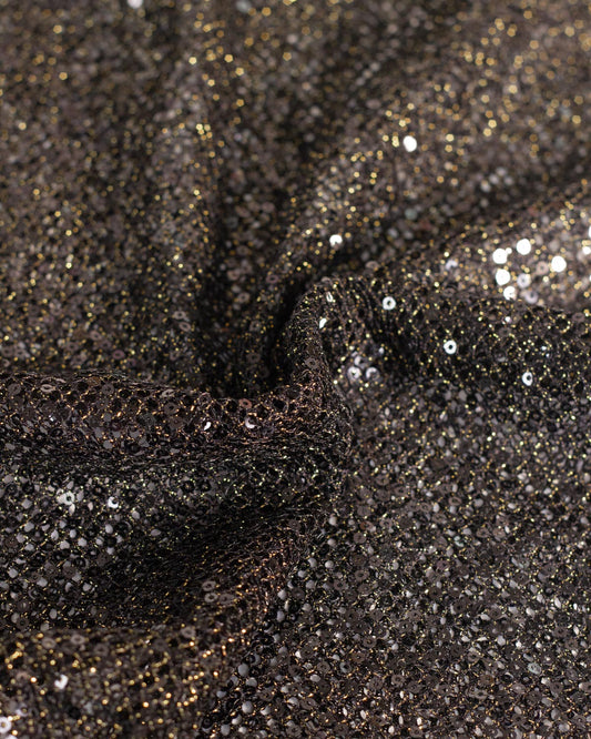 Close-up of a black fishnet tulle fabric with shimmering gold lurex and reflective black sequins, shown in a gathered drape.