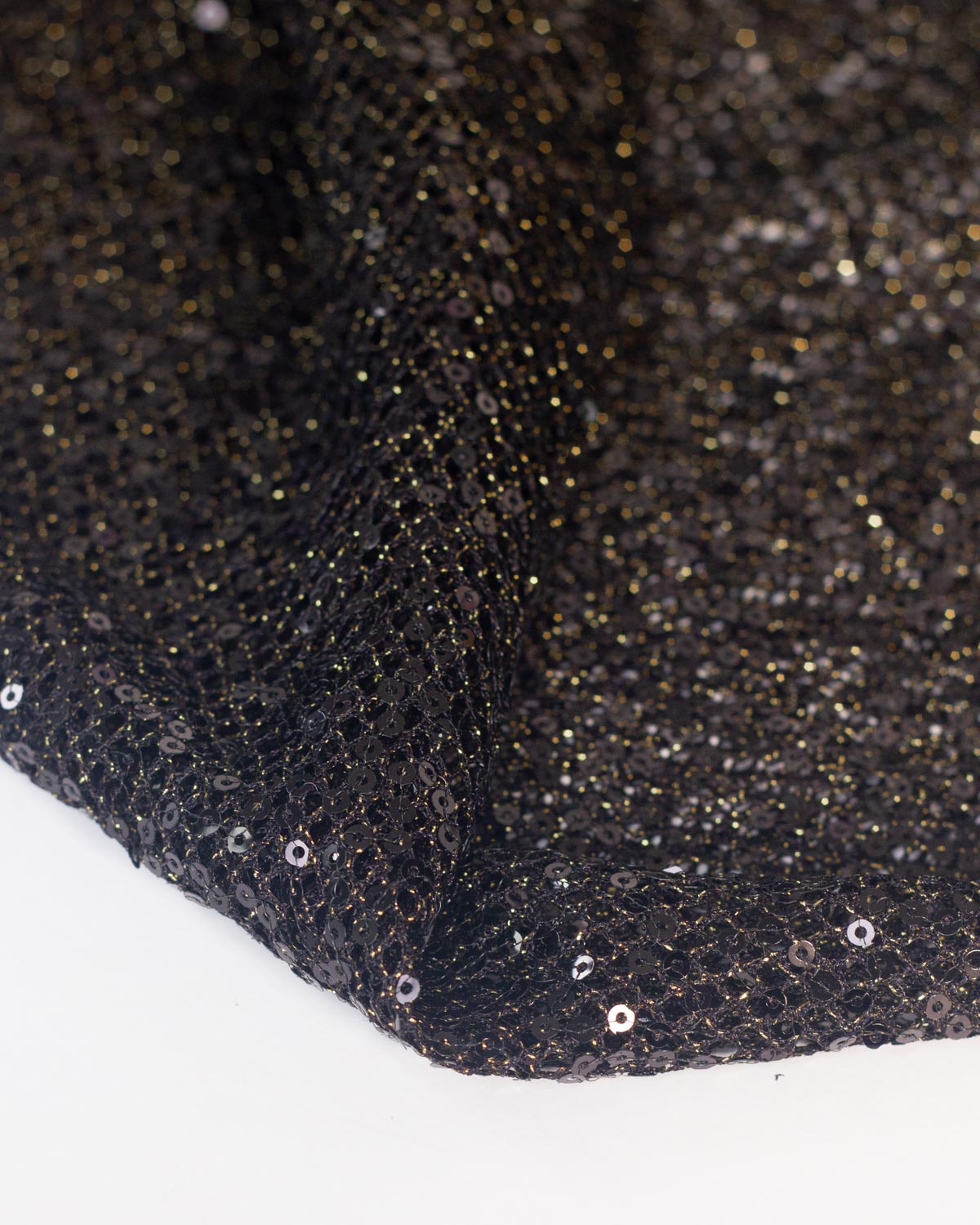 Close-up of a black fishnet tulle fabric with shimmering gold lurex and black reflective sequins, folded over on a white background.