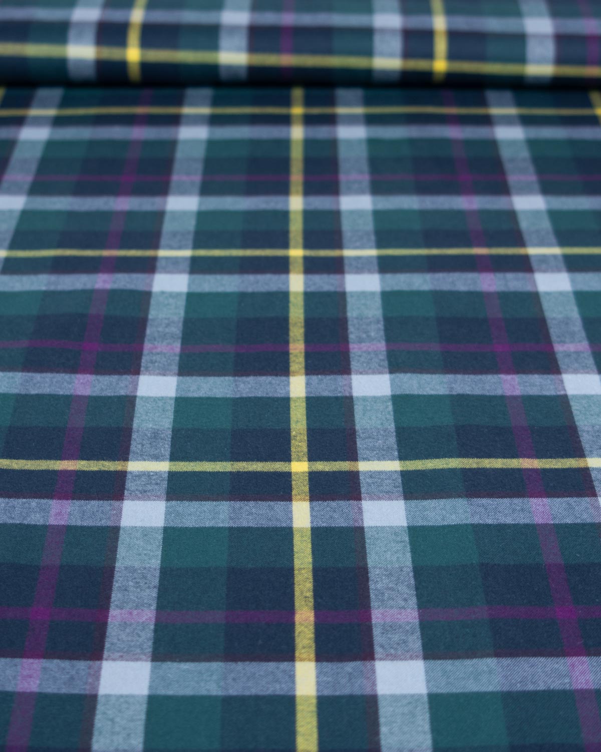 A close-up of a plaid fabric with a tartan pattern in dark green, navy, light blue, purple, and yellow.