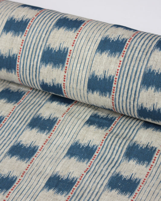 A close-up of a rolled piece of upholstery fabric with a blue and cream ikat pattern, accented by thin red dotted vertical lines.