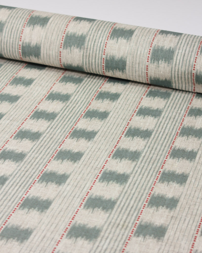 A close-up of linen upholstery fabric showing a repeating ikat-style design in muted sage green and off-white, with thin red dotted accent lines running vertically