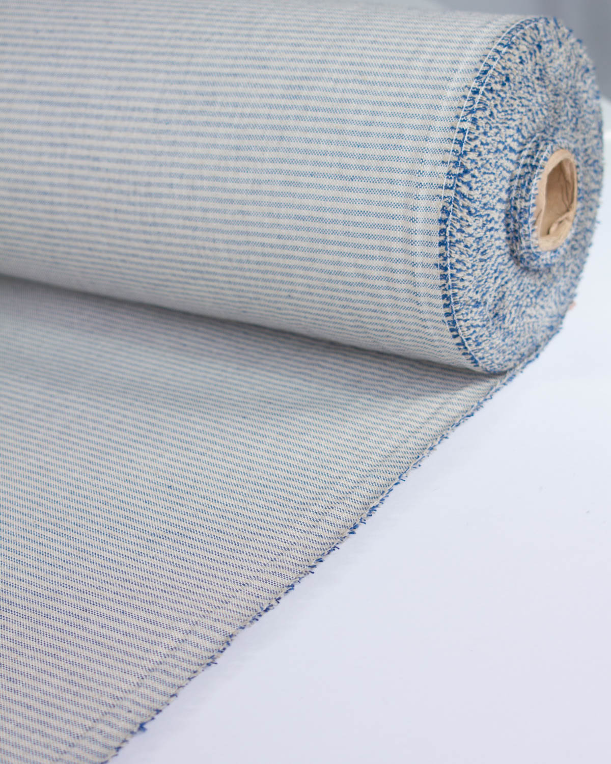 A close-up of a rolled woven curtain fabric or mat with a fine beige and blue stripe