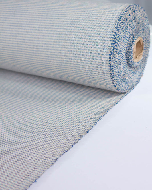 A close-up of a rolled woven curtain fabric or mat with a fine beige and blue stripe