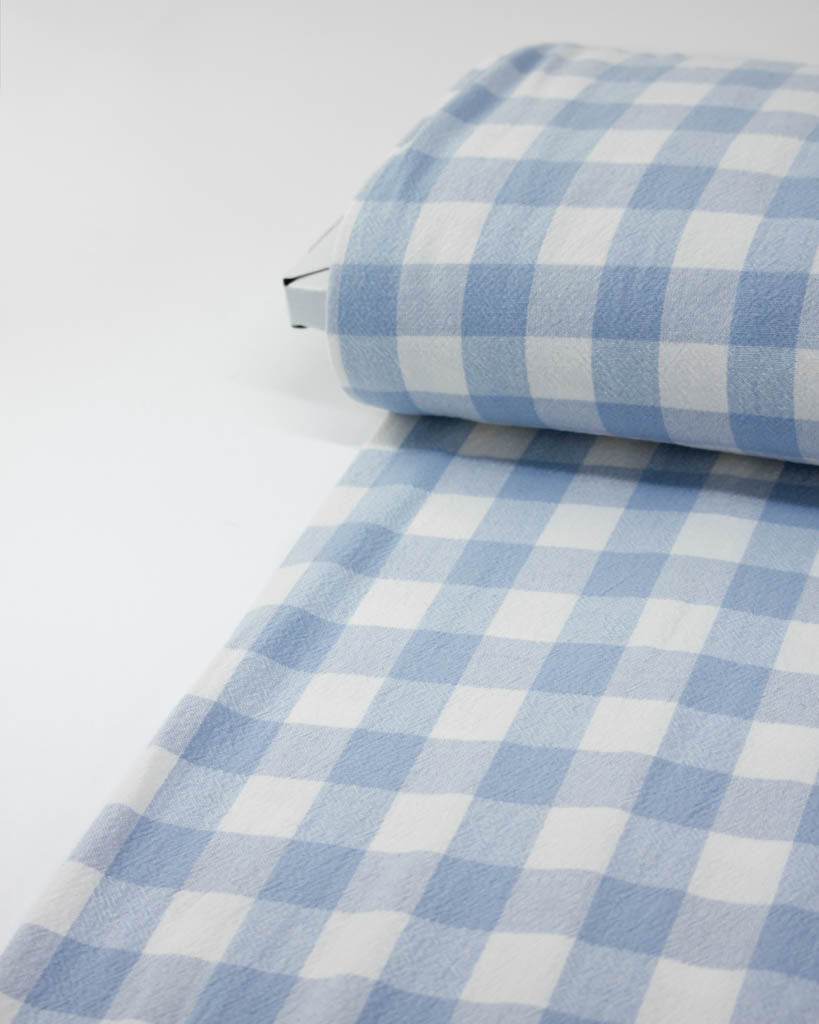 Roll of blue and white checkered gingham cotton fabric on a white background