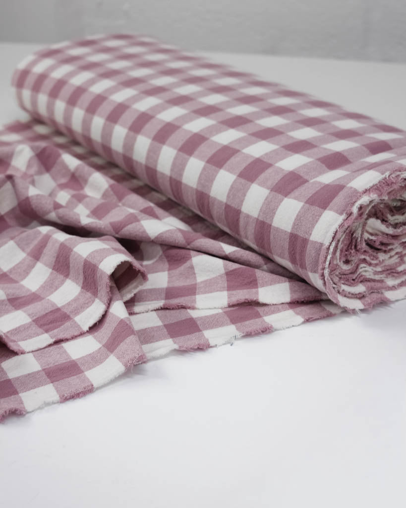 Roll of pink and white checkered gingham cotton fabric on a light gray background