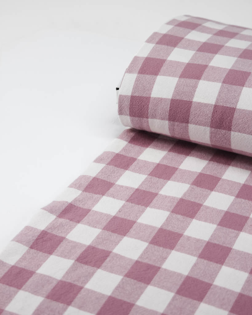 Roll of pink and white checkered gingham cotton fabric on a white background