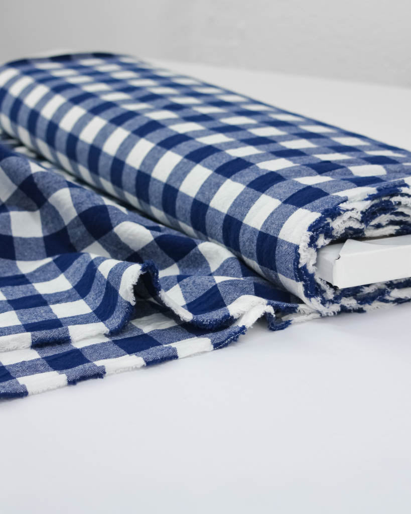 Bolt of Blue and white gingham checkered cotton fabric on a light gray background