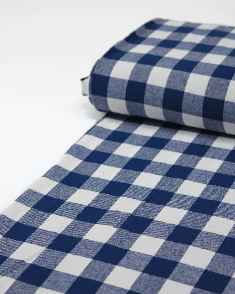 Roll of blue and white checkered gingham cotton fabric on a white background