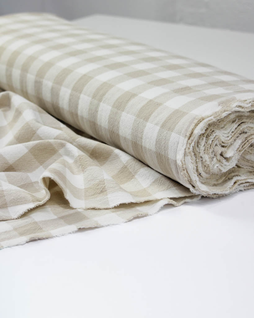 Folded beige and white gingham cotton fabric on a white surface
