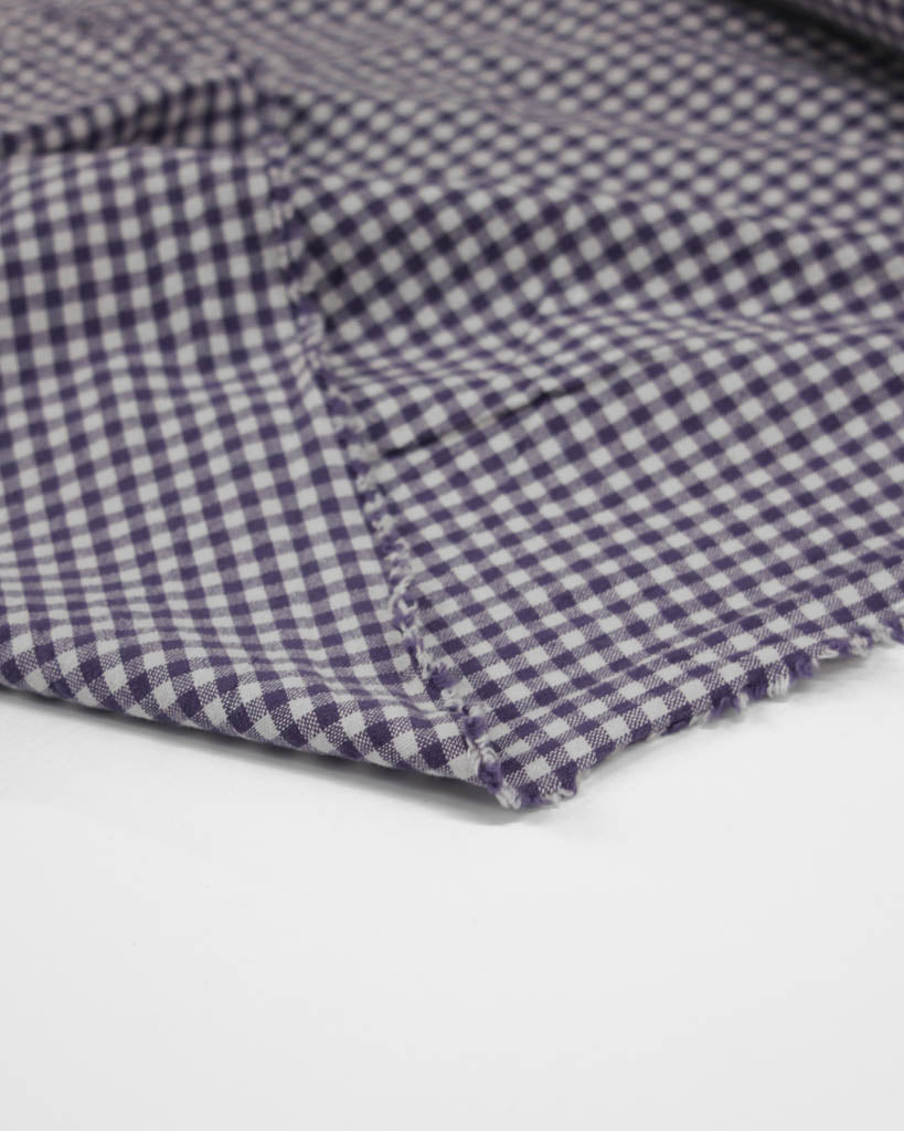 Close-up of a folded purple and white checkered gingham cotton fabric on a light gray background