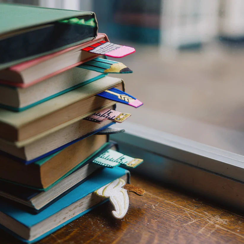 Stack of books with colourful fabric bookmarks on a wooden surface