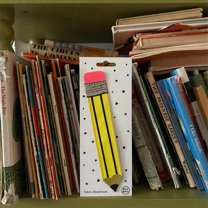 Fabric bookmark with yellow pencil design in packaging on a bookshelf