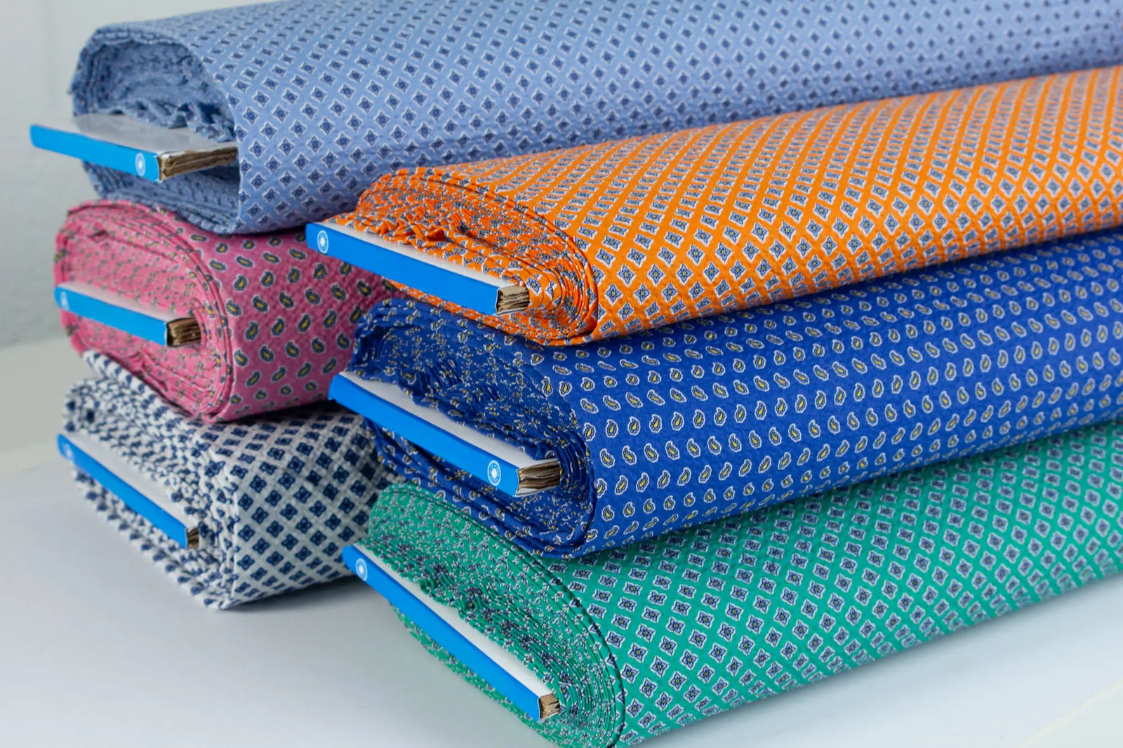 Stack of summer patterned cotton seersucker fabrics in various bright colours on a white background