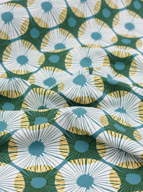 Patterned ruby star society canvas fabric with green, yellow, and blue design on a white background