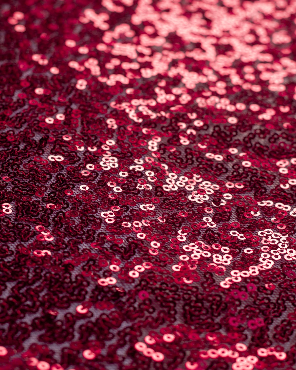 Close-up of a dark ruby red sequined polyester tulle fabric with shimmering red reflective sequins.