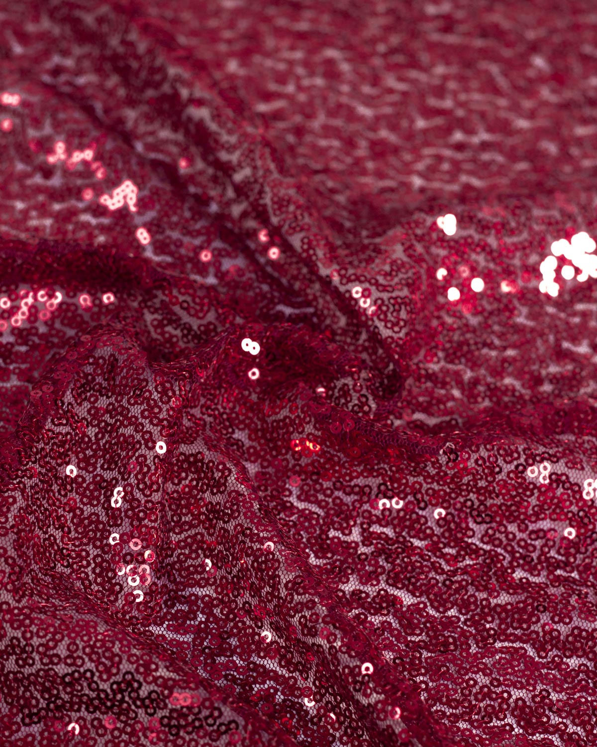 A close-up of deep ruby red tulle fabric with shimmering red reflective sequins draped in soft folds.