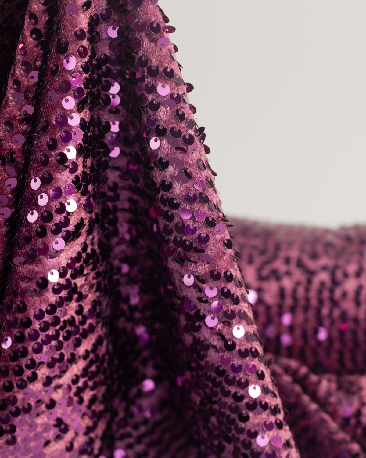 Close-up of draped purple sequined velour stretch fabric with shiny round purple sequins on a white background.