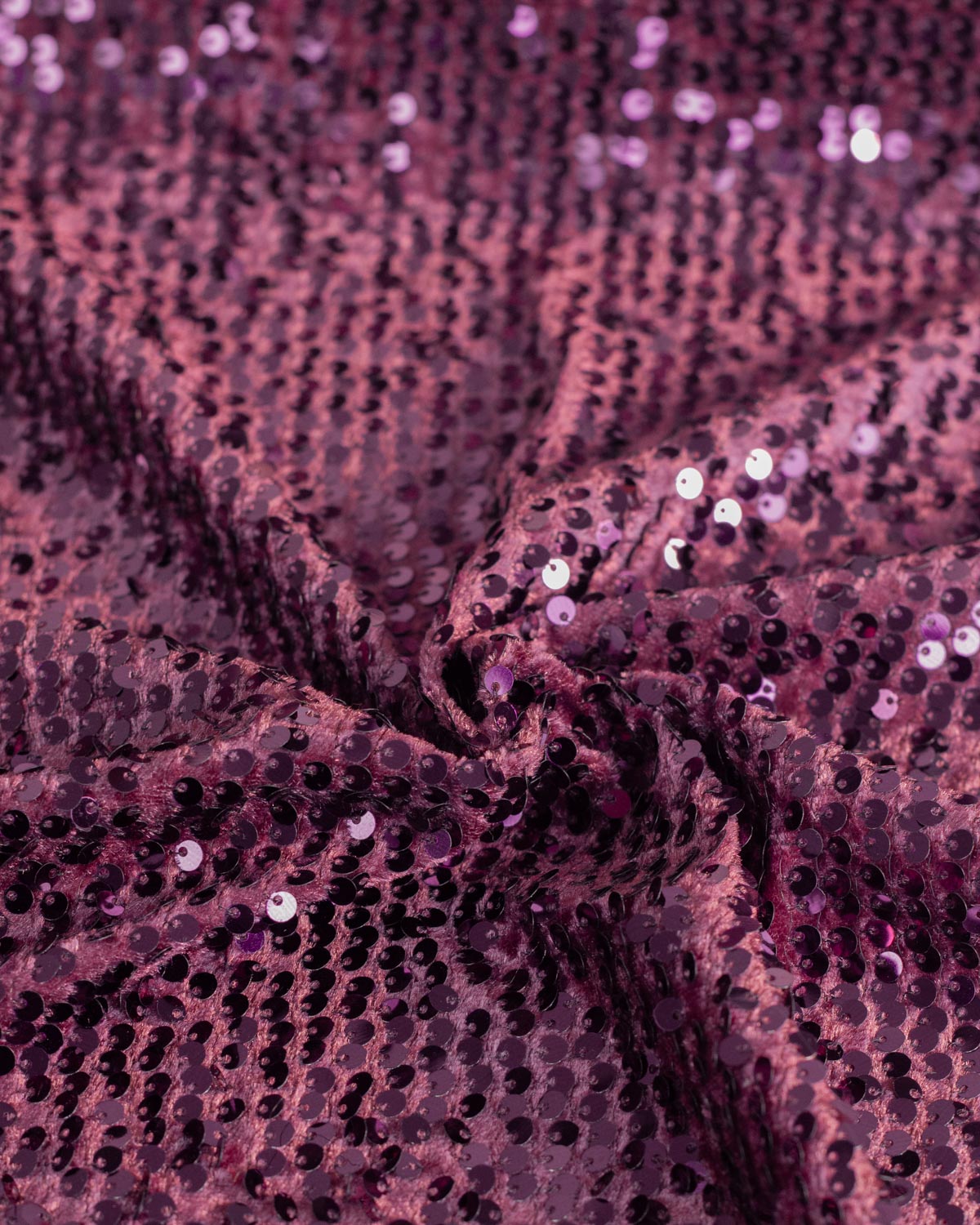 A close-up of draped sequined velour fabric in a deep aubergine purple color, showing the texture and reflective sequins.