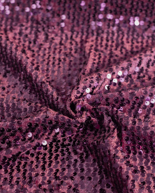 A close-up of draped sequined velour fabric in a deep aubergine purple color, showing the texture and reflective sequins.
