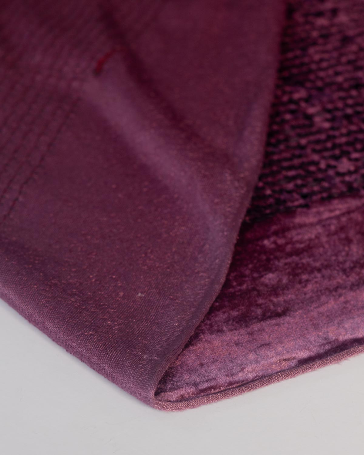 A close-up of a deep aubergine sequined purple velour stretch fabric, showing a  textured velvety underside folded on a white surface. 