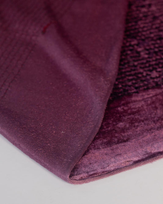 A close-up of a deep aubergine sequined purple velour stretch fabric, showing a  textured velvety underside folded on a white surface. 
