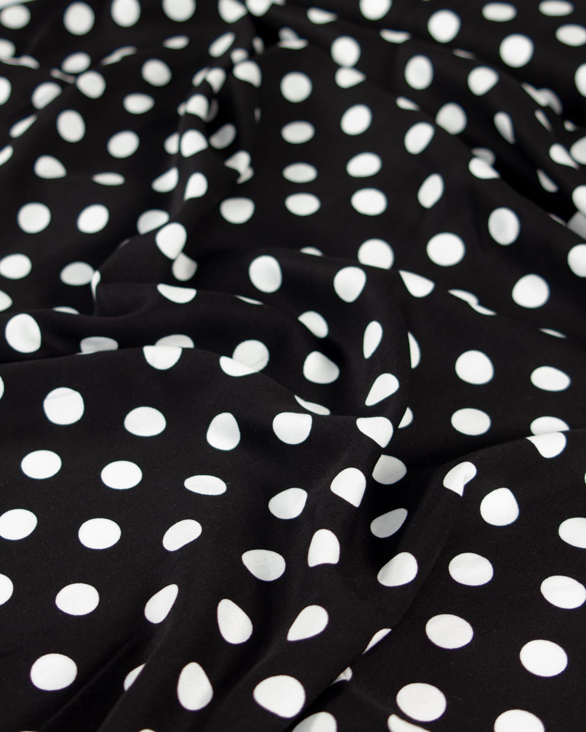 Black viscose twill fabric with a white polka dot pattern, shown with soft folds and ripples.