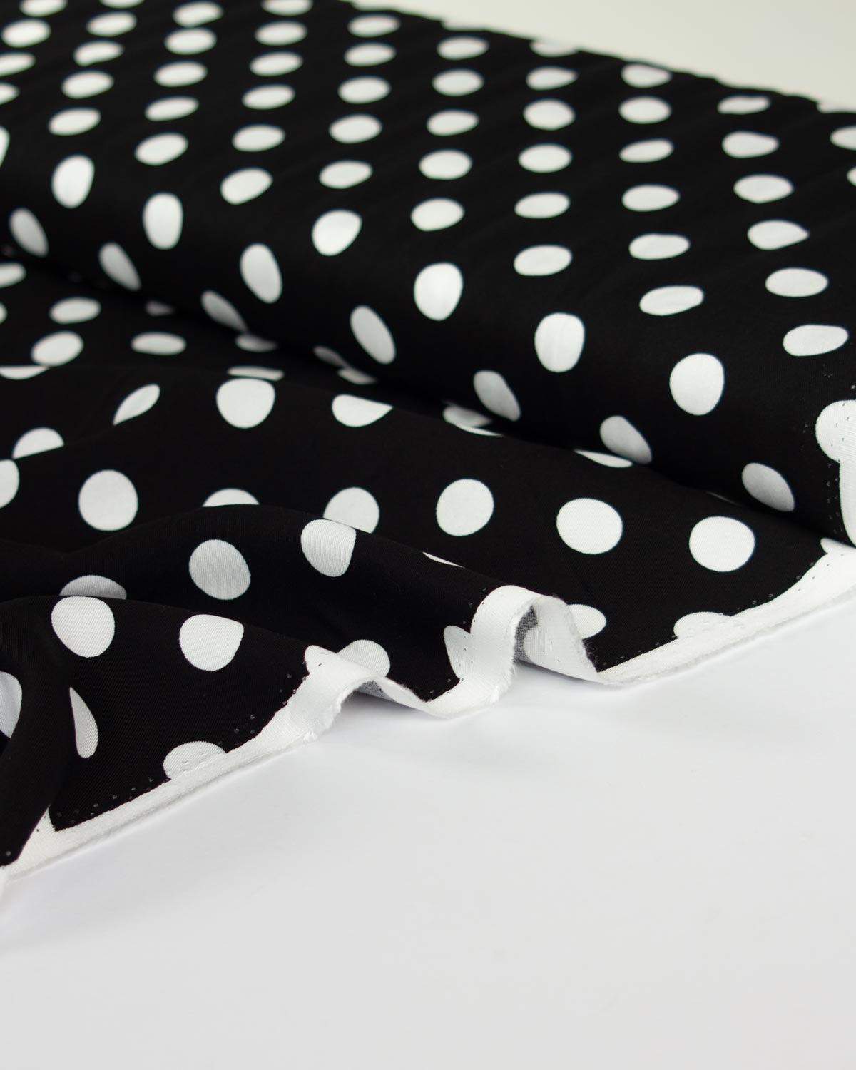 Black viscose twill fabric with a white polka dot pattern, draped to show its texture and white edge trim.