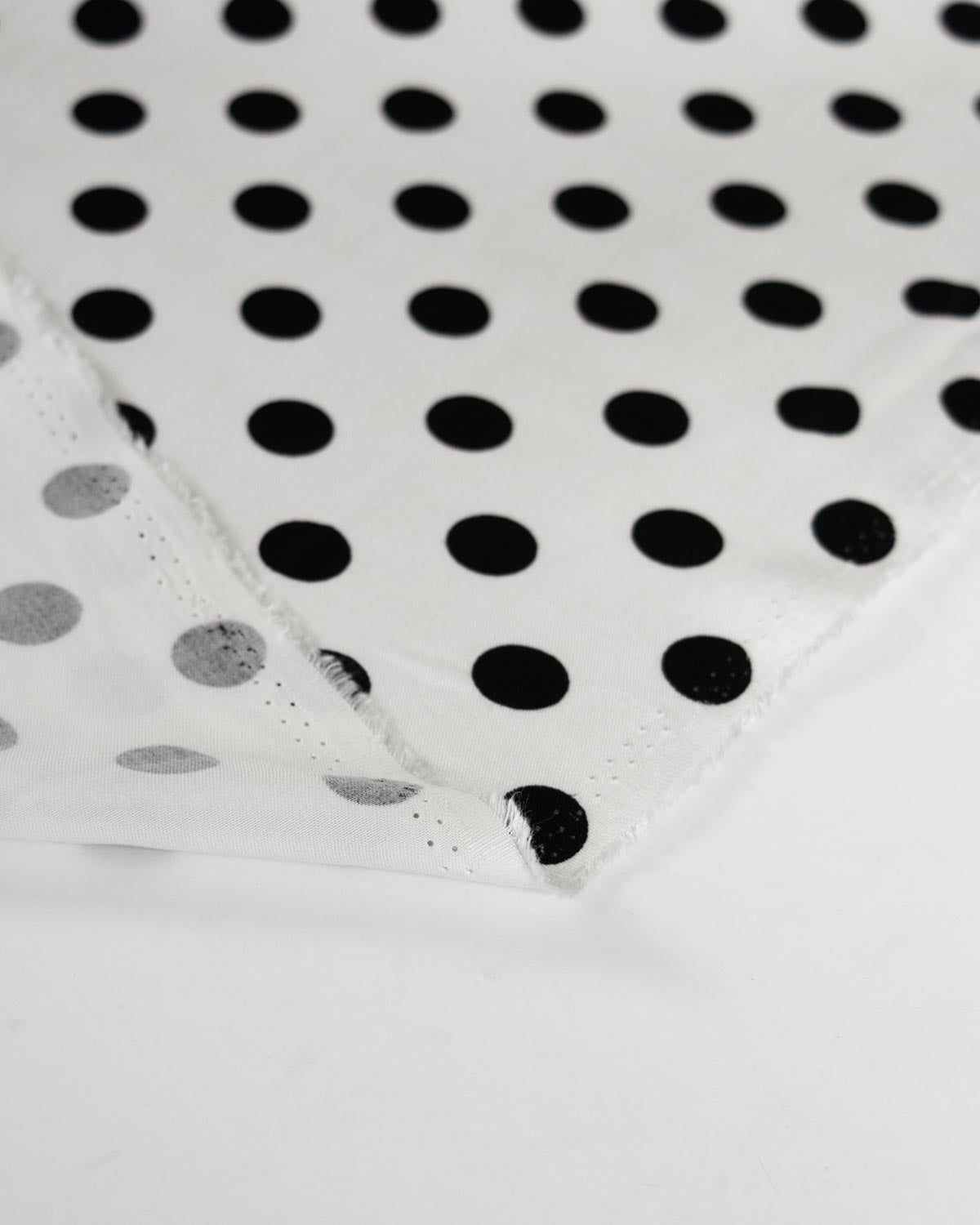 White viscose twill fabric with a black polka dot pattern, folded to show its texture and selvedge.