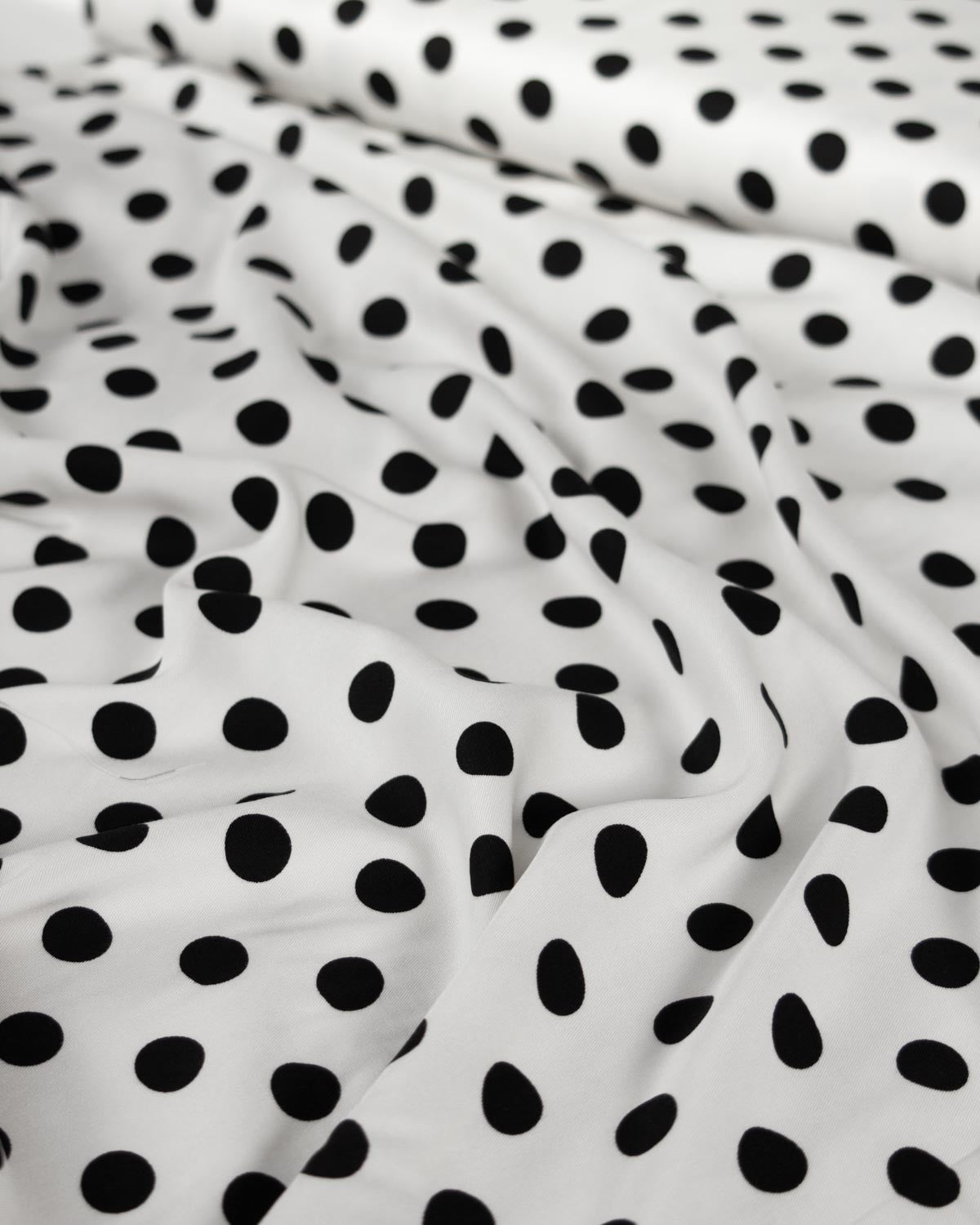 White viscose twill fabric with a black polka dot pattern, shown in soft folds.