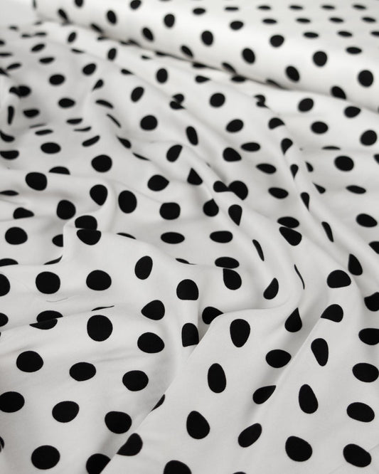White viscose twill fabric with a black polka dot pattern, shown in soft folds.