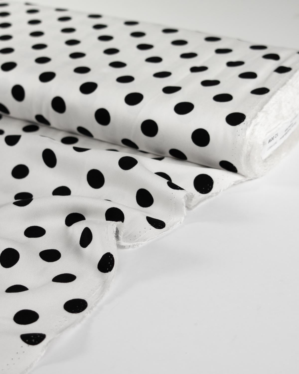 White viscose twill fabric with a black polka dot pattern, shown folded with a roll on a clean white background.