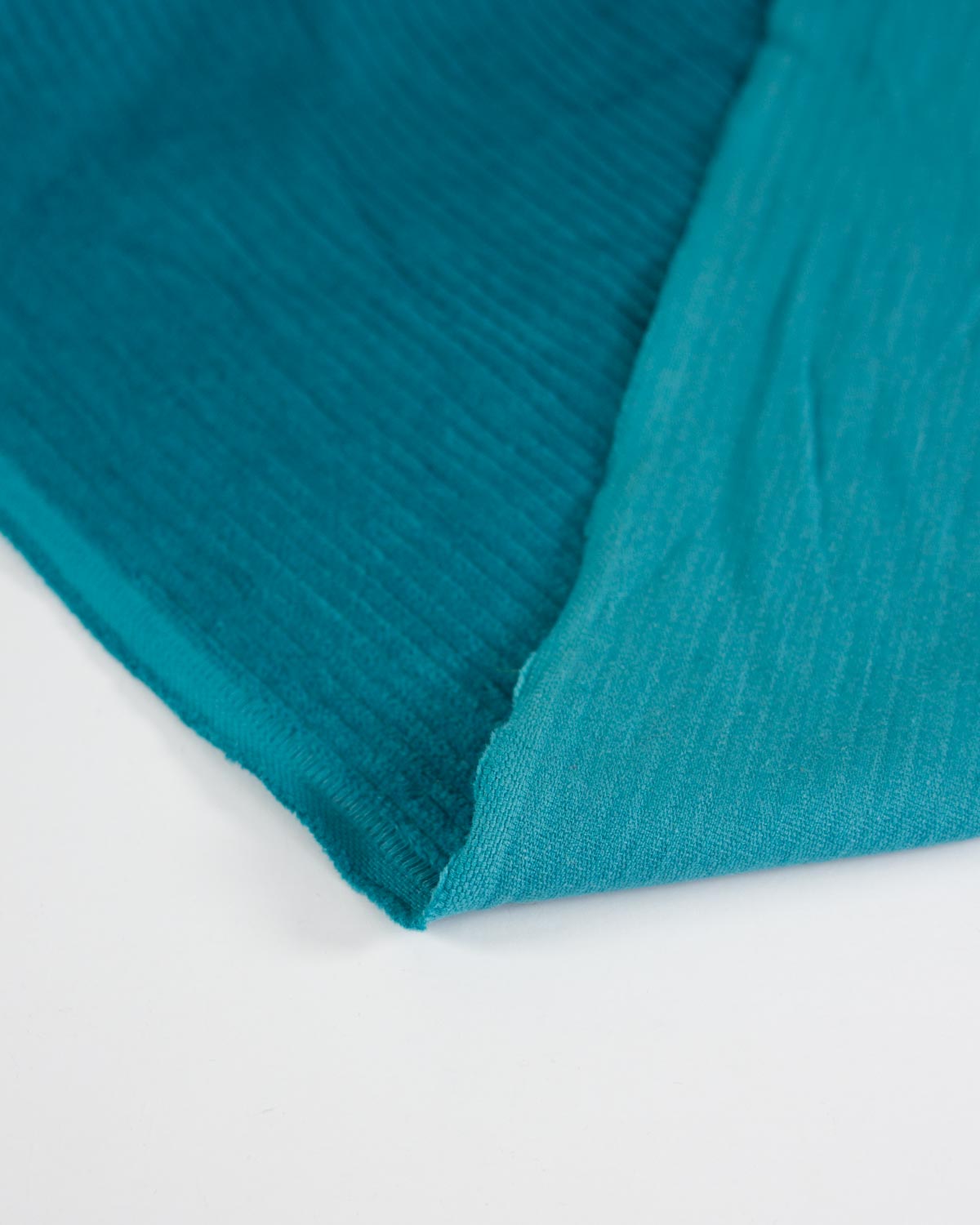 A close-up of a teal corduroy fabric folded over on a plain white background, showing its textured surface and color.